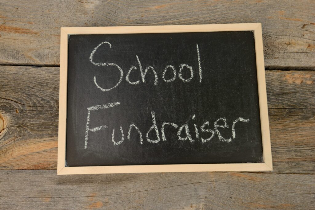 A chalkboard displaying the words "School Fundraiser" in white chalk on a rustic wooden background.