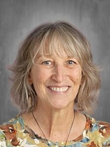 A smiling woman with medium-length wavy hair, wearing a colorful floral shirt, against a gray background.
