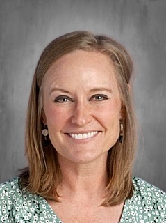 Smiling woman with shoulder-length brown hair, wearing a green patterned blouse and earrings, against a gray background.
