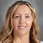 A smiling woman with long, wavy hair wearing hoop earrings and a striped shirt, against a gray background.