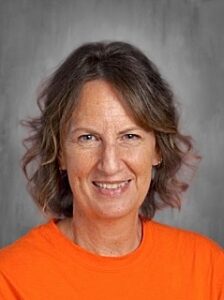 Smiling woman with shoulder-length hair wearing an orange shirt, set against a gray background.