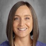 Smiling woman with shoulder-length brown hair, wearing a purple shirt, against a gray background.