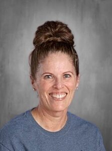 Smiling woman with a bun hairstyle, wearing a gray t-shirt, against a plain gray background.