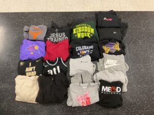 A flat lay of assorted folded sweatshirts and hoodies in various colors and designs, arranged neatly on a black surface.