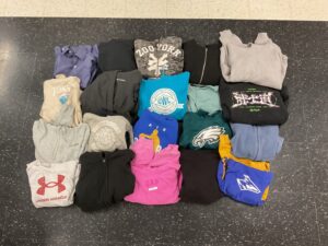 A flat lay of various folded sweatshirts and hoodies in different colors and styles on a black floor.