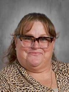 Mujer con gafas, sonriendo, con un top con estampado de leopardo, sobre un fondo gris.