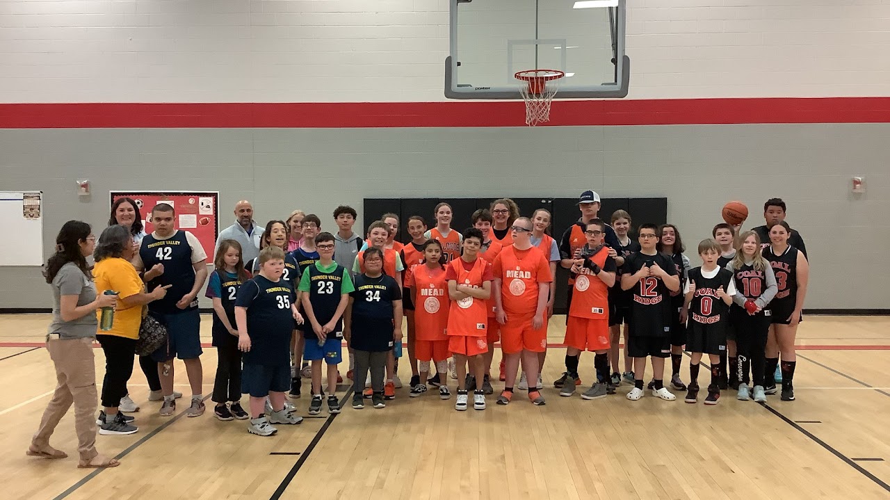 Un grupo variado de niños y adultos posa juntos en una cancha de baloncesto, con las camisetas del equipo puestas y sonriendo.