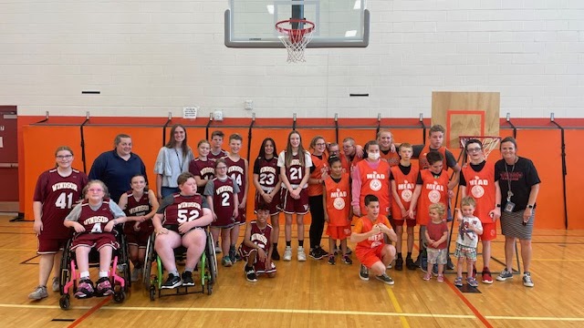 Un grupo variado de jóvenes deportistas posa en un gimnasio, vestidos con camisetas de baloncesto, sonriendo para una foto de equipo.